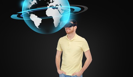 3d technology, virtual reality, entertainment and people concept - happy young man in virtual reality headset or 3d glasses with earth or planet hologram over black backgroundの写真素材