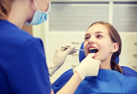 people, medicine, stomatology and health care concept - happy female dentist with mirror checking patient girl teeth up at dental clinic officeの写真素材