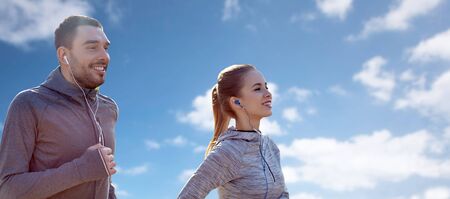 fitness, sport, people, technology and lifestyle concept - happy couple running and listening to...