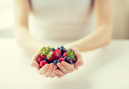 healthy eating, dieting, vegetarian food and people concept - close up of woman hands holding berries at homeの写真素材