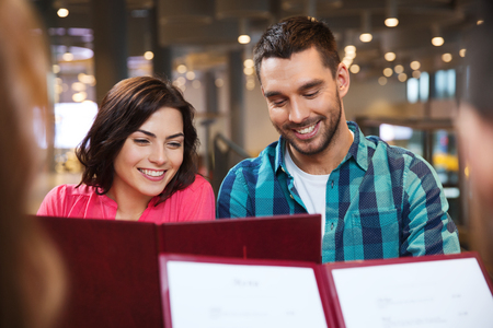 leisure, people and holidays concept - smiling couple with friends reading menu at restaurantの写真素材