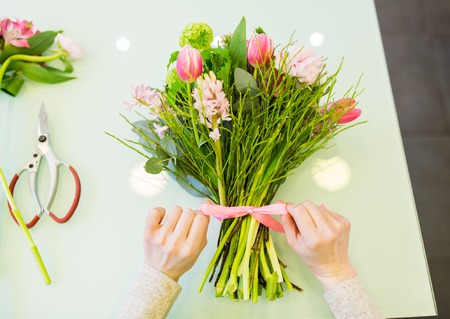 people, business, sale and floristry concept - close up of florist woman making bunch at flower shopの写真素材