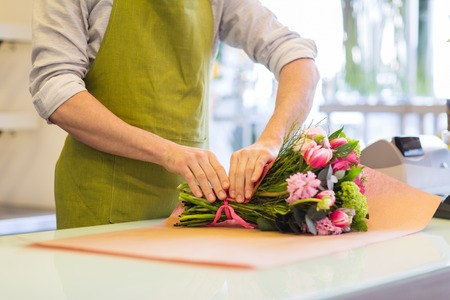 people, shopping, sale, floristry and consumerism concept - close up of florist man wrapping flowers in paper at flower shopの写真素材