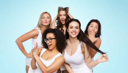 friendship, beauty, body positive and people concept - group of happy plus size women in white underwear having fun and making faces over blue backgroundの写真素材