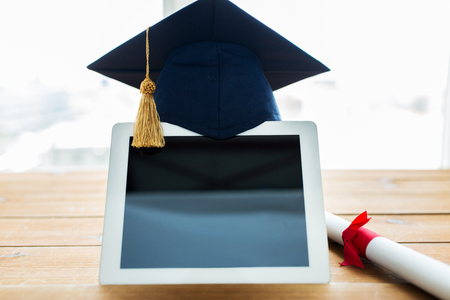 education, graduation, technology and e-learning concept - close up of tablet pc computer with mortarboard and diploma scroll on wooden tableの写真素材