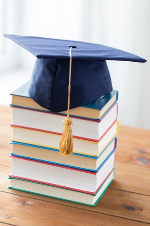 education, school, graduation and knowledge concept - close up of books and mortarboard on wooden tableの写真素材