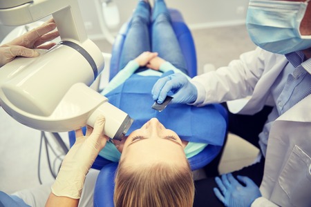 people, medicine, stomatology, technology and health care concept - close up of dentist putting intraoral shield to female patient mouth and assistant directing x-ray machine at dental clinicの写真素材