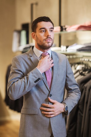 sale, shopping, fashion, business style and people concept - elegant young man choosing and trying on suit and tie in mall or clothing storeの写真素材