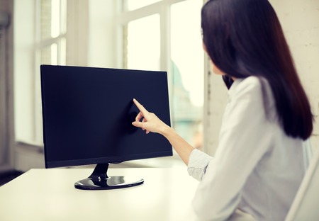 business, people, technology and education concept - close up of woman pointing finger to computer monitor in officeの写真素材