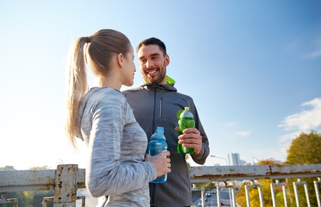 fitness, sport, friendship and lifestyle concept - smiling couple with bottles of water outdoorsの写真素材