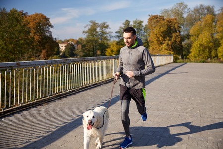fitness, sport, people, pets and jogging concept - happy man with labrador retriever dog running outdoorsの写真素材