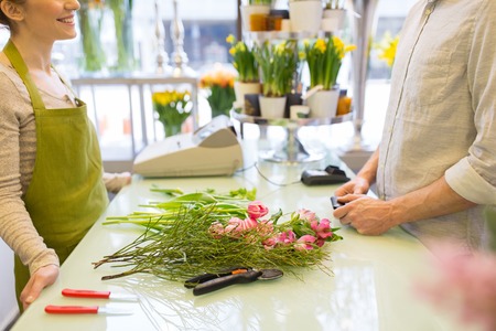 people, shopping, sale, floristry and consumerism concept - close up of happy florist woman making bouquet for and man or customer at flower shopの写真素材