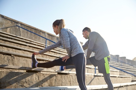 fitness, sport, exercising and lifestyle concept - couple stretching leg on stands of stadium