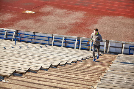 fitness, sport, exercising and people concept - happy young man running upstairs on stadiumの写真素材