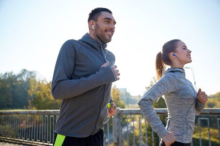 fitness, sport, people and lifestyle concept - happy couple with earphones running outdoorsの写真素材