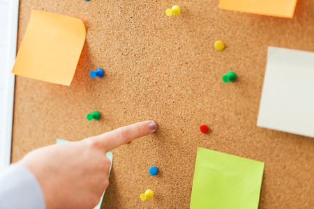 office, business, people and education concept - close up of hand pointing to to cork board with stickers and office pinsの写真素材