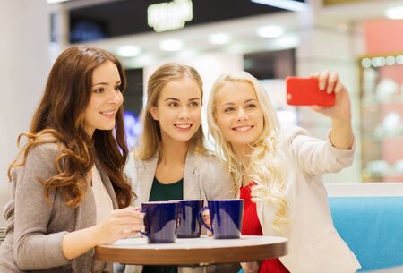 drinks, friendship, technology and people concept - happy young women with cups sitting at table and...
