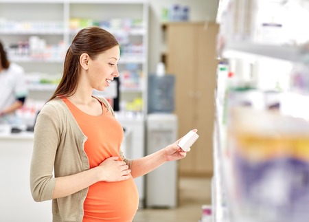 pregnancy, medicine, pharmaceutics, health care and people concept - happy pregnant woman with medication at pharmacyの写真素材