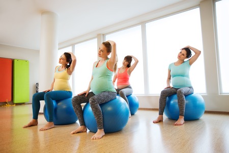 pregnancy, sport, fitness, people and healthy lifestyle concept - group of happy pregnant women exercising on ball in gymの写真素材
