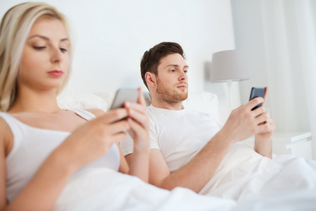 people, technology, internet and communication concept - couple with smartphones in bedの写真素材