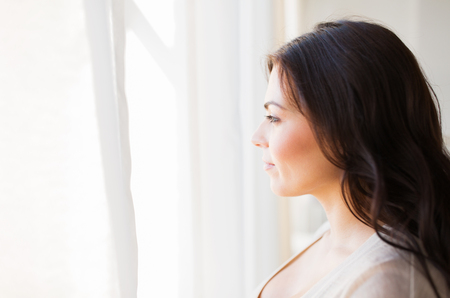 people and leisure concept - young woman looking through window at homeの写真素材