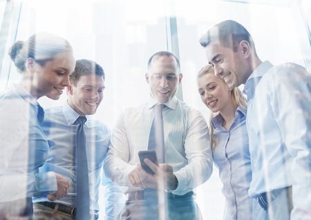 business, teamwork, people and technology concept - business team looking to smartphone in officeの写真素材