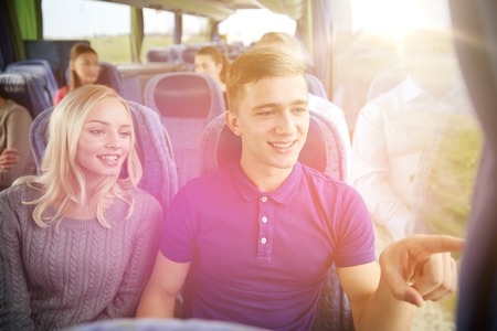 transport, tourism, road trip and people concept - happy teenage couple with group of passengers or tourists in travel busの写真素材