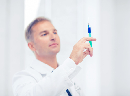 healthcare and medical concept - male doctor holding syringe with injectionの写真素材