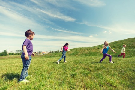 summer, childhood, leisure and people concept - group of happy kids playing tag game and running on green field outdoorsの写真素材