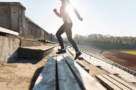 fitness, sport, exercising and people concept - close up of young woman running upstairs on stadiumの写真素材