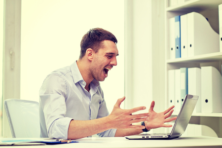 business, people, stress, fail and technology concept - angry businessman with laptop computer and papers shouting in officeの写真素材