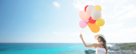 travel, tourism, summer, holidays and people concept - smiling young woman wearing sunglasses with balloons over exotic tropical beach and sea backgroundの写真素材