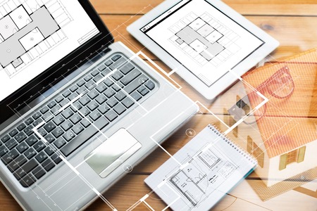 architecture, business and technology concept - close up of on laptop computer, tablet pc, notebook and eyeglasses with blueprint of room on wooden tableの写真素材