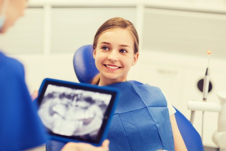 people, medicine, stomatology, technology and health care concept - dentist with x-ray on tablet pc computer and girl patientの写真素材
