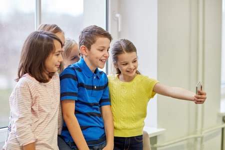 education, elementary school, drinks, children and people concept - group of school kids taking selfie with smartphone in corridorの写真素材
