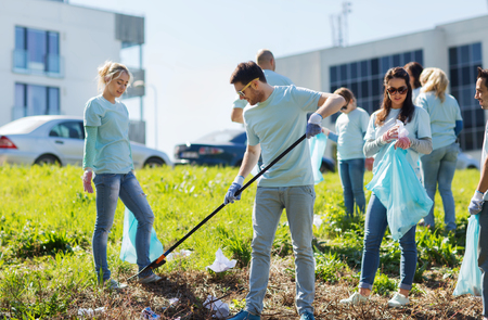 volunteering, charity, cleaning, people and ecology concept - group of happy volunteers with garbage bags cleaning area in park