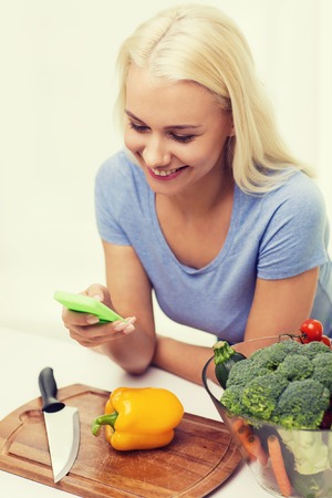 healthy eating, vegetarian food, dieting and people concept - smiling young woman with smartphone cooking vegetables at homeの写真素材