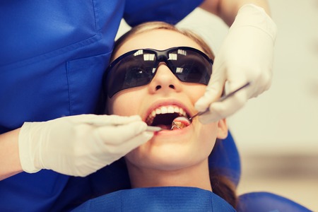 people, medicine, stomatology and health care concept - happy female dentist with mirror and probe checking patient girl teeth up at dental clinic officeの写真素材