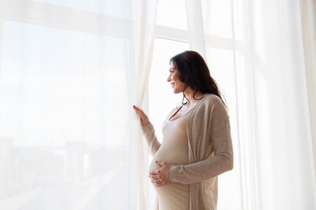 pregnancy, motherhood, people and expectation concept - close up of happy pregnant woman with big belly looking to windowの写真素材