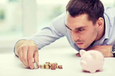 business, people, finances and money saving concept - businessman with piggy bank and coins at officeの写真素材