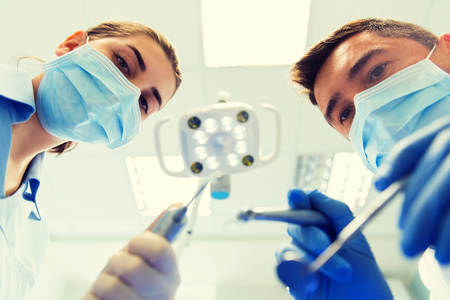 people, medicine, stomatology and health care concept - close up of dentist and assistant with dental mirror, drill and air water gun spray treating patient teeth at dental clinicの写真素材