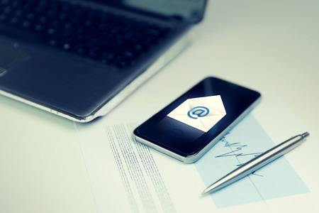 business, technology and communication concept - close up of smartphone with email message icon , laptop computer and chart with pen on office tableの写真素材