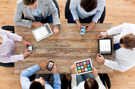 business, people, technology, media and team work concept - close up of creative team with smartphones and tablet pc computers sitting at table in officeの写真素材