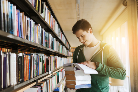 people, knowledge, education, literature and school concept - happy student or young man with book in libraryの写真素材