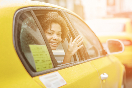 business trip, transportation, travel, gesture and people concept - young smiling african american woman driving in taxi and waving hand at city streetの写真素材