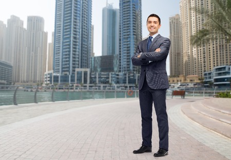 business, people and office concept - happy smiling businessman in dark grey suit over dubai city street backgroundの写真素材