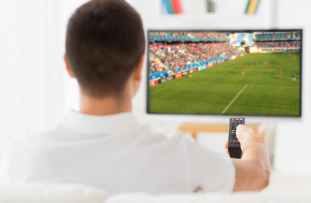 leisure, technology, sport, entertainment and people concept - man with remote control watching football or soccer game on tv at homeの写真素材