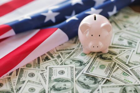 budget, finance, saving and nationalism concept - close up of american flag, piggy bank and dollar cash moneyの写真素材