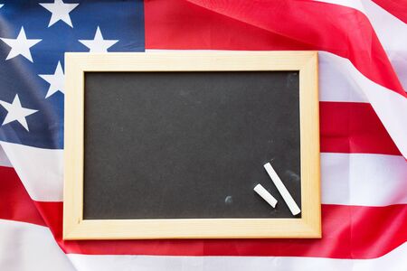 education, election, patriotism and nationalism concept - close up of blank school blackboard and chalk on american flagの写真素材