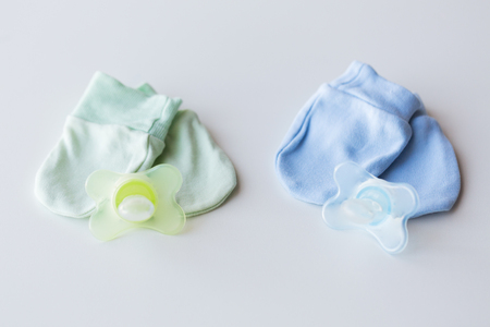 clothing, babyhood, accessory and object concept - close up of baby mittens and soothers for newborn twinsの写真素材